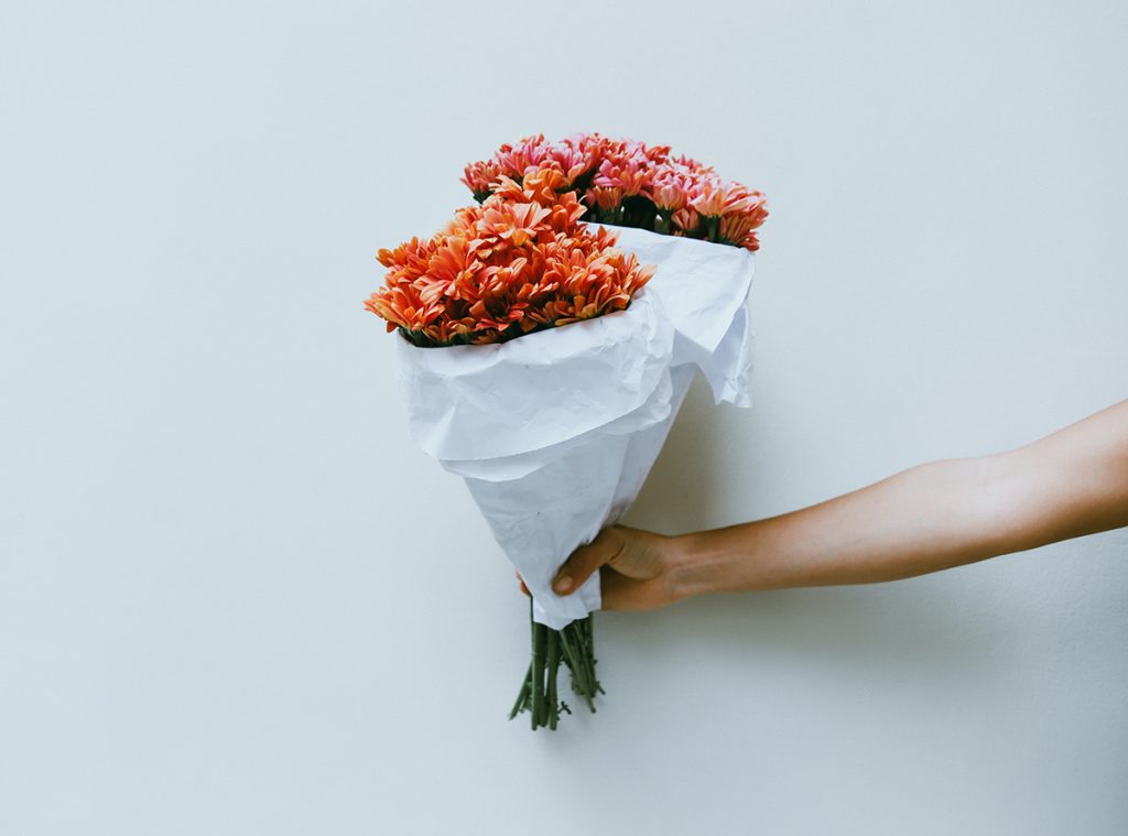 Hand holding out bouquets of pink and coral colored flowers