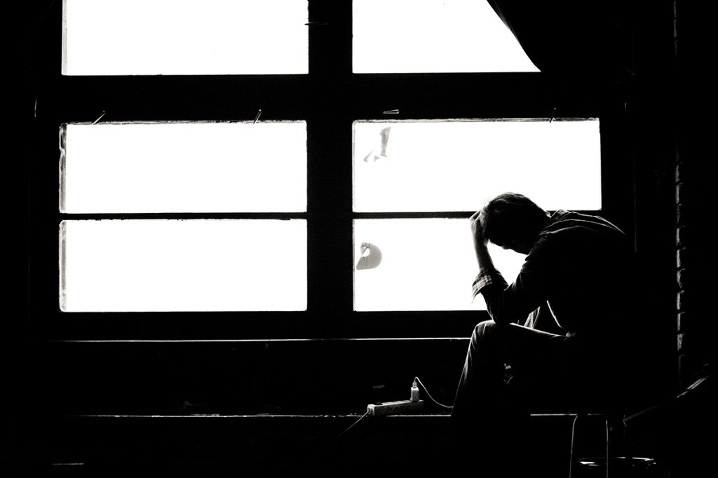 Man experiencing worry shown in silhouette against a brightly lit window; black & white photo