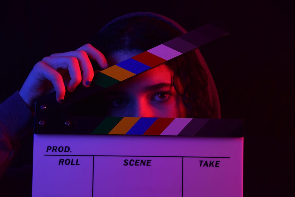 Close up of a woman obscuring her face with a film clapboard in purple light