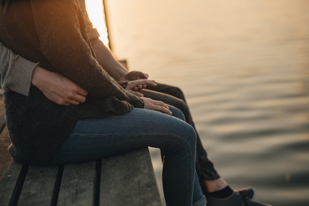 Couple sitting on a dock, pictured from the waist down, at sunset