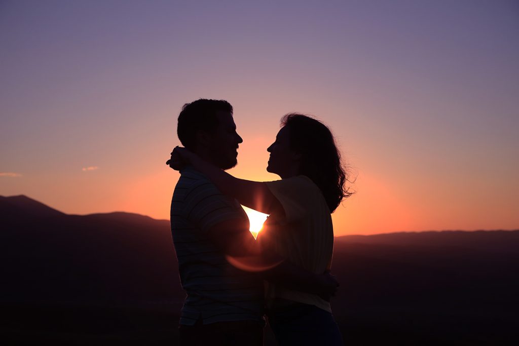 embracing couple silhouetted against a sunset