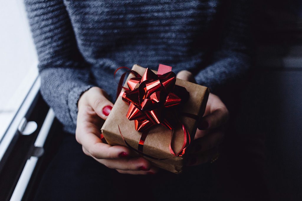 woman's hands holding a small gift wrapped with a red bow